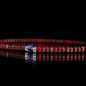 Può includere: Un braccialetto di perline rosse con un unico accento di pietra preziosa viola.