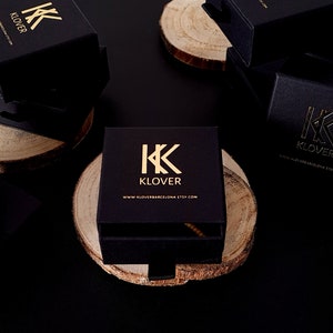 Może przedstawiać: Czarne pudełka na biżuterię ze złotym napisem. Pudełka mają logo "KK KLOVER" i adres strony internetowej "www.kloverbcn.etsy.com".