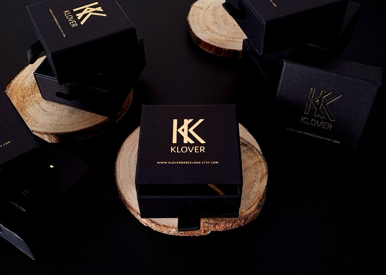 Może przedstawiać: Czarne pudełka na biżuterię ze złotym napisem. Pudełka mają logo "KK KLOVER" i adres strony internetowej "www.kloverbcn.etsy.com".