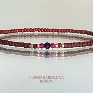 Peut inclure: Un bracelet rouge en perles avec un accent noir, rose et argent. Le bracelet est sur une surface blanche avec le texte "KLOVER BARCELONA JEWELRY" en dessous.