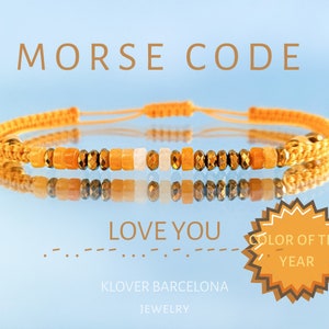 Puede incluir: Un brazalete de cuentas amarillas y marrones con el mensaje "LOVE YOU" en código Morse. El brazalete está hecho por KLOVER BARCELONA JEWELRY y está etiquetado como "COLOR OF THE YEAR".