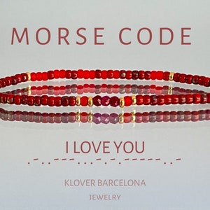 Op de afbeelding: Rode kralen armband met gouden kralen en een kleine rode edelsteen. De armband spelt "IK HOU VAN JE" in morsecode.