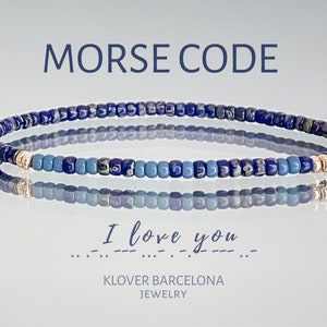 Puede incluir: Un brazalete de cuentas azules y blancas con detalles dorados. El brazalete deletrea "Te amo" en código Morse.