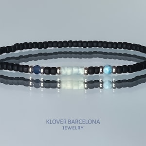 Puede incluir: Un brazalete de cuentas negras con cuentas de piedras preciosas azules y blancas. El brazalete está sobre un fondo blanco.