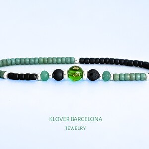 May include: A green and black beaded bracelet with a green glass bead with gold lettering, a black lava bead, and two green jade beads.