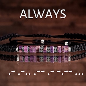 Puede incluir: Dos pulseras trenzadas negras con detalles morados y plateados. La palabra "ALWAYS" se muestra encima de las pulseras. Debajo, una serie de puntos y rayas en código Morse.