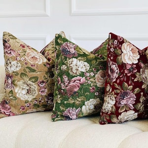 May include: Four decorative throw pillows with floral patterns in various colors, including beige, green, burgundy, and cream. The pillows are arranged on a white sofa, showcasing a classic, elegant design.