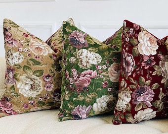 May include: Four decorative throw pillows with floral patterns in various colors, including beige, green, burgundy, and cream. The pillows are arranged on a white sofa, showcasing a classic, elegant design.