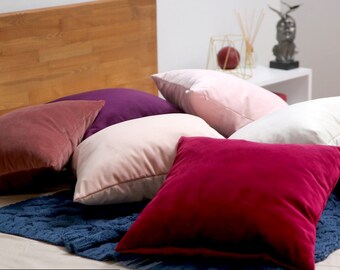 May include: A collection of decorative throw pillows in various colors, including pink, burgundy, and white. The pillows are arranged on a bed with a blue knitted throw blanket. The text "THE Lucca luxury COLLECTION" is visible at the bottom of the image.