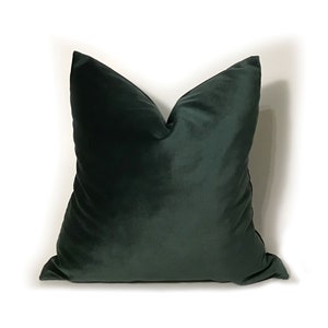May include: A dark green velvet pillow with a square shape. The pillow is made of a soft, plush fabric.