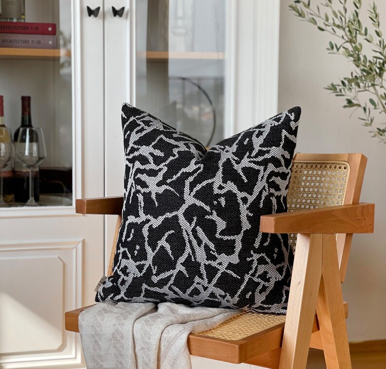 May include: A black and white patterned throw pillow with a geometric design sits on a wooden chair with a woven cane seat.