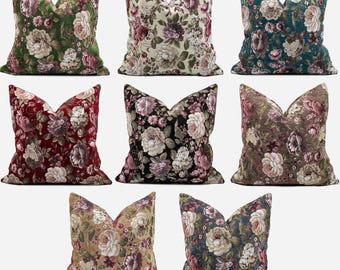 May include: A collection of decorative throw pillows with floral patterns. The pillows feature various color schemes, including green, cream, burgundy, black, and brown, each adorned with detailed flower designs. The pillows are square-shaped with a V-shaped top.