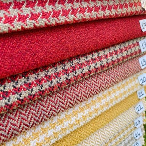 May include: A selection of fabric samples showcasing a range of textures and designs. The swatches feature solid red, red and white herringbone, and yellow and white patterned fabrics. Each fabric is labelled with a small white tag, ideal for upholstery or interior design.