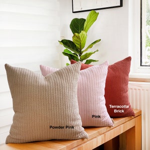 May include: Three decorative throw pillows with a cable knit texture. The pillows are in shades of powder pink, pink, and terracotta brick.