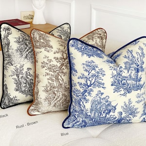 May include: Decorative throw pillows with toile scenes in black, rust-brown, and blue. Each pillow features a contrasting border: black, rust-brown, and blue. The pillows are on a white sofa. The pillows have a classic, elegant design.