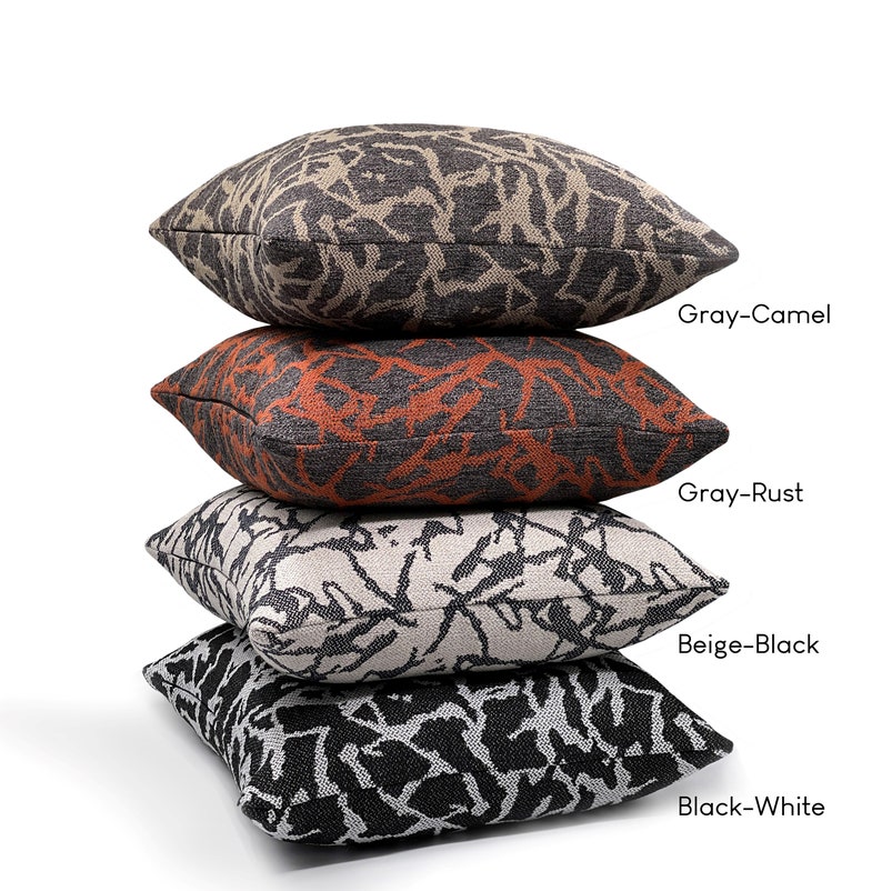 May include: Four decorative throw pillows stacked on top of each other. The pillows are made of a textured fabric with a black and white abstract pattern. The top pillow is gray with a camel colored pattern, the second pillow is gray with a rust colored pattern, the third pillow is beige with a black pattern, and the bottom pillow is black with a white pattern. The pillows are labeled with their color combinations: Gray-Camel, Gray-Rust, Beige-Black, and Black-White.
