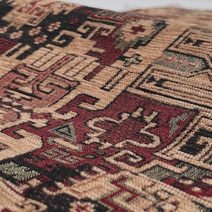 May include: A woven fabric featuring a dense, intricate geometric pattern in shades of deep red, black, and tan. The textile displays repeating angular motifs and interconnected shapes across its textured surface, creating a complex visual design.
