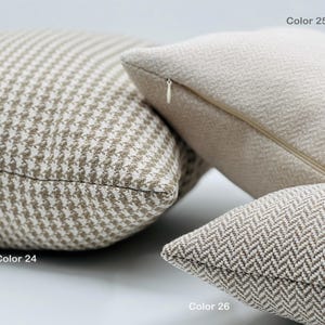 May include: Three throw pillows in different patterns and colors. The pillow on the left is a brown and white houndstooth pattern. The pillow in the middle is a solid off-white color. The pillow on the right is a brown and white herringbone pattern. The pillows are labeled "Color 24", "Color 25", and "Color 26".