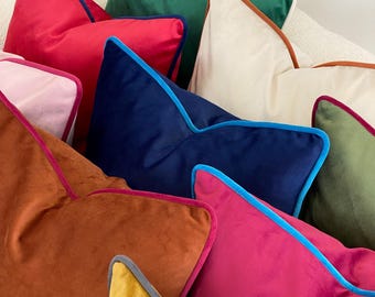 Könnte beinhalten: Eine Sammlung bunter Samt-Kissen mit kontrastierenden Paspeln. Die Kissen sind in einem Stapel angeordnet und zeigen eine Vielzahl von Farben, darunter Rosa, Rot, Grün, Blau, Orange und Gelb.