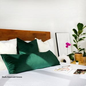 May include: A bed with white bedding and two dark emerald green velvet pillows. The bed has a wooden headboard and a white throw blanket on the side.