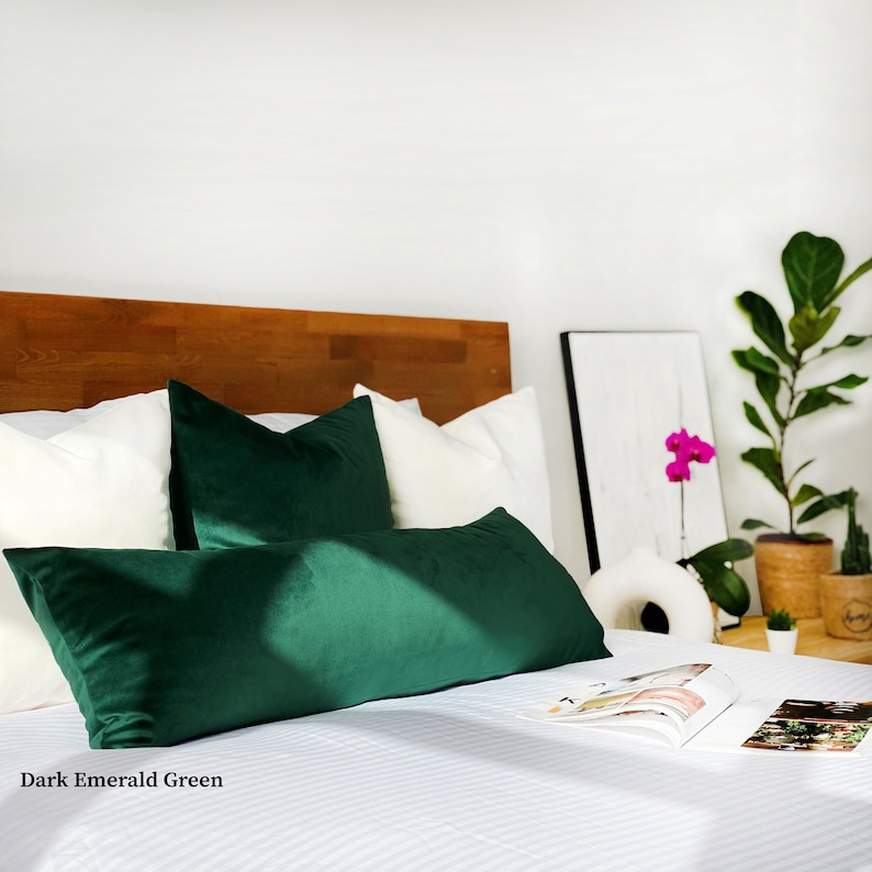 May include: A bed with white bedding and two dark emerald green velvet pillows. The bed has a wooden headboard and a white throw blanket on the side.