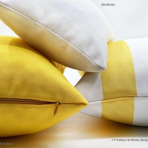 Op de afbeelding: Close-up van verschillende decoratieve sierkussens in verschillende kleuren en patronen. E&eacute;n kussen is effen geel met een gouden rits, een ander is wit en een derde heeft gele en witte strepen. De tekst op de afbeelding luidt "16-Yellow", "28-White" en "17-Yellow & White Stripe".