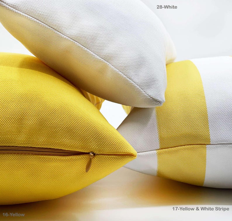 Op de afbeelding: Close-up van verschillende decoratieve sierkussens in verschillende kleuren en patronen. E&eacute;n kussen is effen geel met een gouden rits, een ander is wit en een derde heeft gele en witte strepen. De tekst op de afbeelding luidt "16-Yellow", "28-White" en "17-Yellow & White Stripe".
