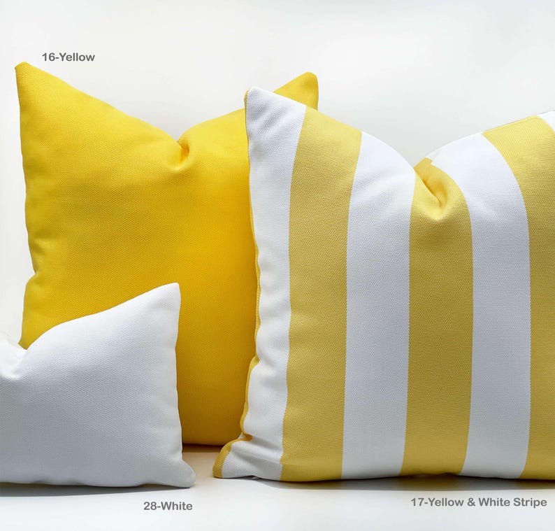 Op de afbeelding: Een verzameling decoratieve kussens in verschillende kleuren en patronen. De kussens omvatten effen gele, witte en geel-wit gestreepte ontwerpen. De kussens zijn gelabeld met hun kleur- of patroonnamen.