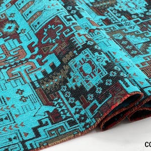 May include: A folded piece of fabric featuring a vibrant turquoise background with intricate geometric patterns in black and deep red. The textile displays a repeating design of interconnected shapes and lines, with the text COLOR 5 visible.