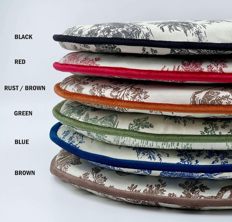 May include: A stack of round cushions with a toile pattern in shades of gray and brown. Each cushion has a different colored border: black, red, rust/brown, green, blue, and brown. The cushions are stacked on top of each other.