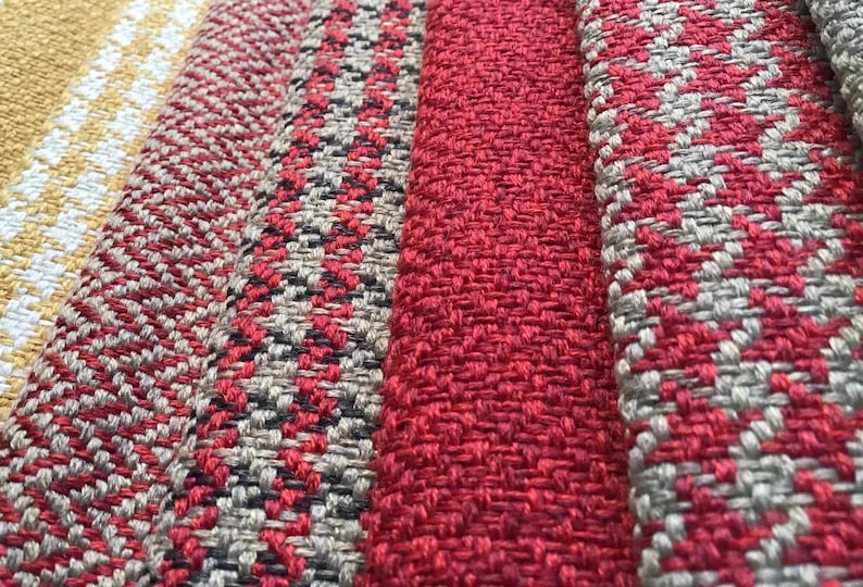 Puede incluir: Primer plano de cuatro muestras de tela con diferentes patrones y colores. Las muestras son rojas, grises, blancas y amarillas.