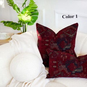 May include: Two red and black patterned throw pillows with geometric designs on a white couch. The pillows are arranged on a white couch with a white throw blanket. The text "Color 1" is visible in the upper right corner of the image.