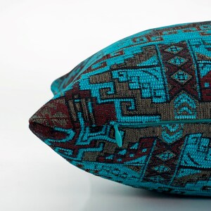 May include: Close-up of a decorative cushion with a teal, brown, and grey geometric pattern. The cushion has a teal zip and a textured fabric. The design features repeating shapes and lines, creating a detailed textile.