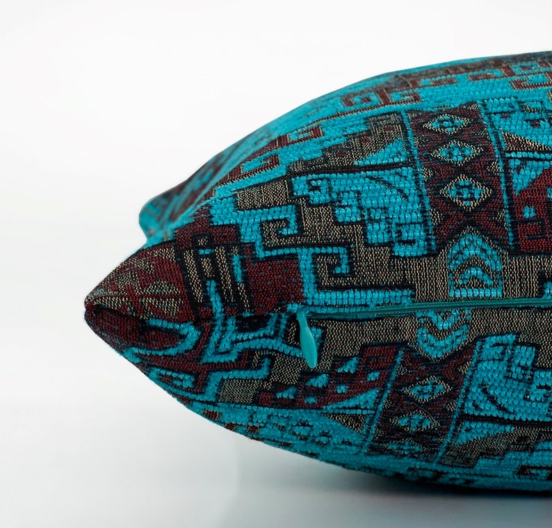 May include: Close-up of a decorative cushion with a teal, brown, and grey geometric pattern. The cushion has a teal zip and a textured fabric. The design features repeating shapes and lines, creating a detailed textile.