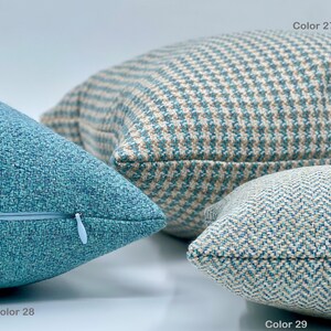 Puede incluir: Tres almohadas decorativas en varios tonos de azul y beige con diferentes patrones. La almohada de la izquierda tiene un color azul s&oacute;lido con una textura sutil. La almohada del medio tiene un patr&oacute;n a cuadros en azul y beige. La almohada de la derecha tiene un patr&oacute;n de espiga en azul y beige. Las almohadas est&aacute;n etiquetadas con los n&uacute;meros de color 28, 27 y 29.