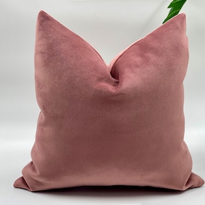 May include: A soft, dusty rose velvet pillow with a square shape. The pillow is made of a plush, velvety fabric and has a simple, elegant design.