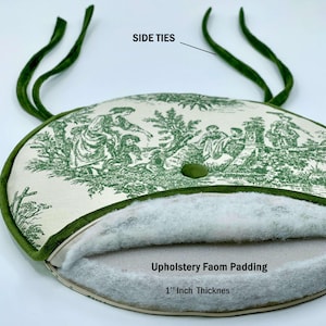 May include: An oval cushion with a green and white toile pattern, featuring a 1-inch thick upholstery foam padding. The cushion has green side ties and a green button. The text "Side Ties" and "Upholstery Foam Padding 1" Inch Thicknes" are visible.