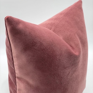 May include: A soft, dusty rose velvet pillow with a subtle sheen. The pillow is square and has a simple, elegant design.