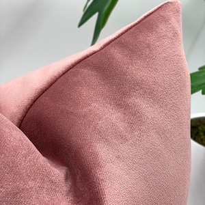May include: A soft, blush pink velvet pillow cover. The fabric has a subtle texture and a smooth finish.