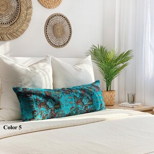 May include: A long, rectangular turquoise cushion with a geometric pattern in brown and gold rests on a bed with white pillows and a cream-coloured blanket. The text "Color 5" is visible in the lower left corner.
