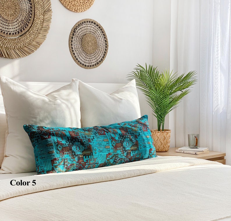 May include: A long, rectangular turquoise cushion with a geometric pattern in brown and gold rests on a bed with white pillows and a cream-coloured blanket. The text "Color 5" is visible in the lower left corner.