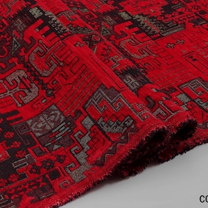 May include: A vibrant red fabric featuring a complex, repeating geometric pattern in black and dark gray. The textile has a textured, woven appearance with visible fibers along the folded edge and the text COLOR 2 in the bottom corner.