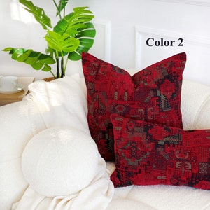 May include: Two decorative throw pillows with a red and black geometric pattern. The pillows are on a white couch with a white throw blanket and a green plant in the background. The text "Color 2" is visible in the top right corner of the image.
