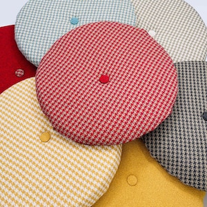 Puede incluir: Una colecci&oacute;n de boinas redondas estampadas en varios colores, incluyendo rojo, amarillo, azul y gris. Cada boina presenta un patr&oacute;n de pata de gallo o similar y un peque&ntilde;o bot&oacute;n a juego en la parte superior. Las boinas est&aacute;n hechas de tela texturizada.