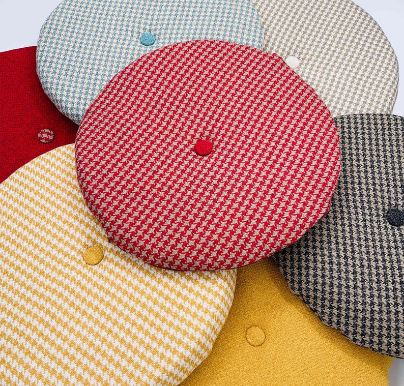 Puede incluir: Una colecci&oacute;n de boinas redondas estampadas en varios colores, incluyendo rojo, amarillo, azul y gris. Cada boina presenta un patr&oacute;n de pata de gallo o similar y un peque&ntilde;o bot&oacute;n a juego en la parte superior. Las boinas est&aacute;n hechas de tela texturizada.