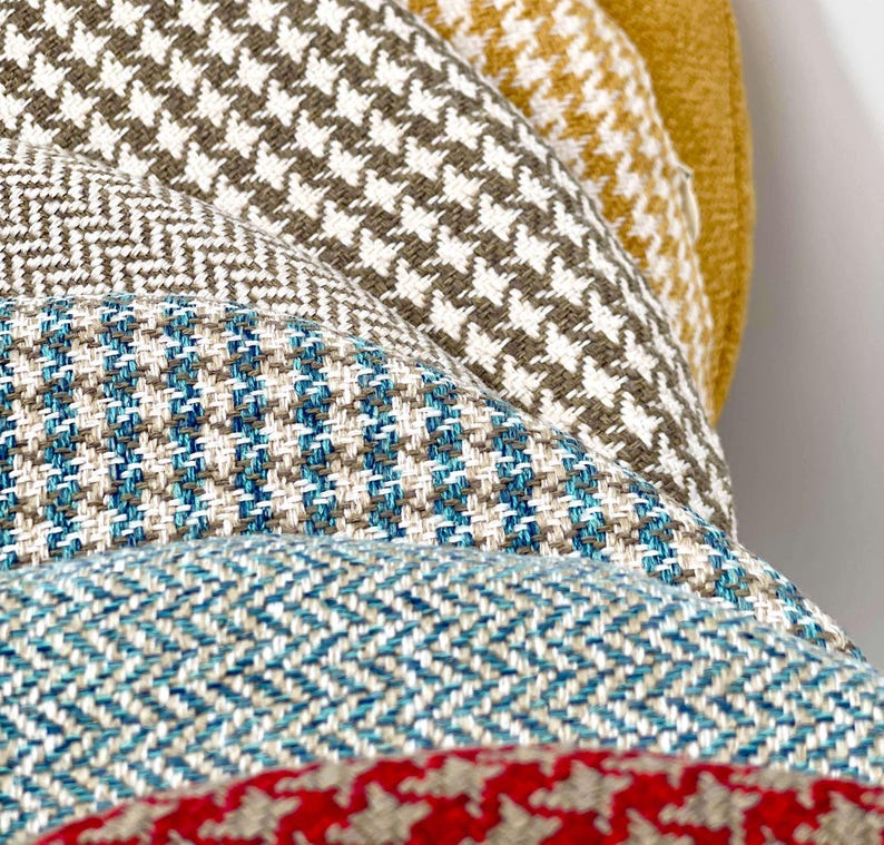 Puede incluir: Primer plano de una pila de telas estampadas en varios colores. Las telas incluyen pata de gallo, espiga y otros dise&ntilde;os tejidos en tonos marrones, azules, blancos y rojos. Adecuado para tapicer&iacute;a o decoraci&oacute;n del hogar.