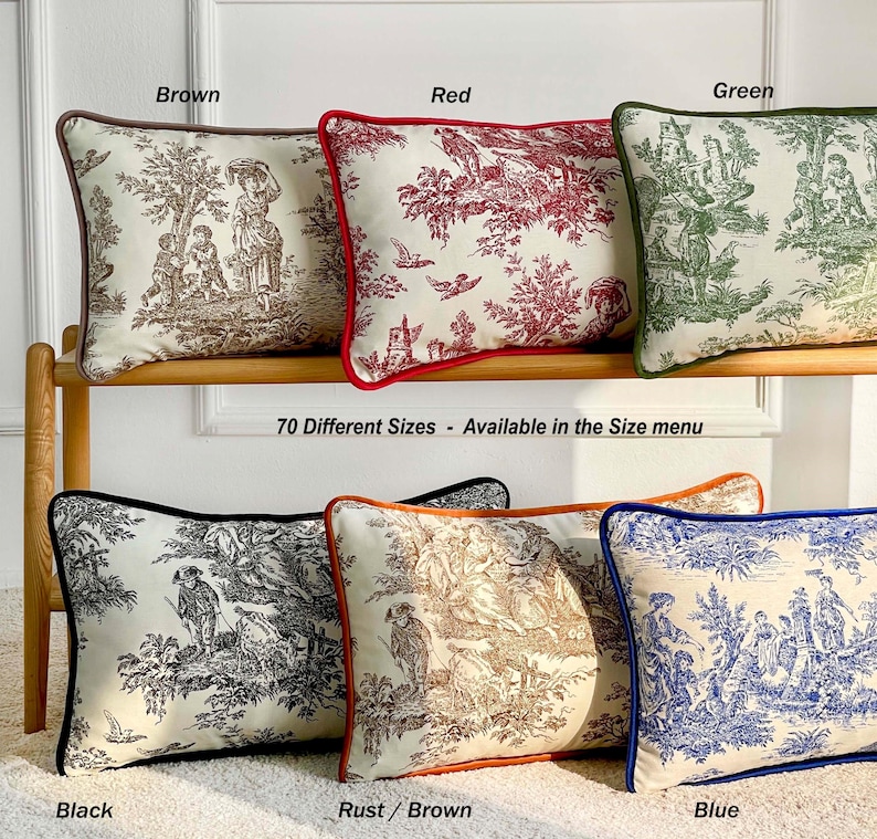 K&ouml;nnte beinhalten: Dekorative Zierkissen in verschiedenen Farben, darunter Braun, Rot, Gr&uuml;n, Schwarz, Rostbraun und Blau. Jedes Kissen zeigt ein Toile-de-Jouy-Muster mit einem kontrastierenden Rand. Der Text "70 Different Sizes - Available in the Size menu" ist zu sehen.
