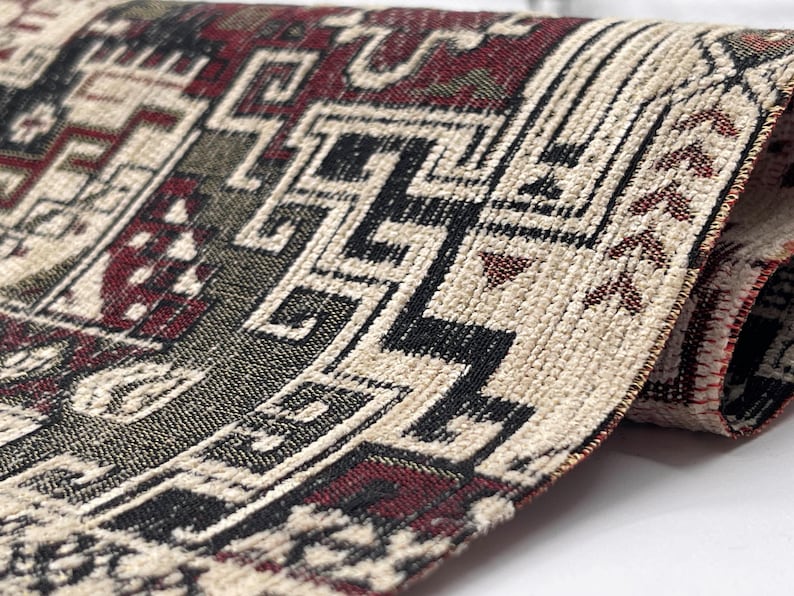 May include: A woven textile fabric featuring a complex geometric pattern in deep red, black, and cream colors. The material has a textured surface with visible interlaced threads forming intricate angular shapes and repeating motifs.