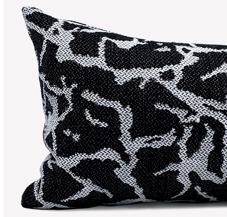 May include: Black and white patterned throw pillow with a geometric design. The pillow is made of a woven fabric and has a rectangular shape.