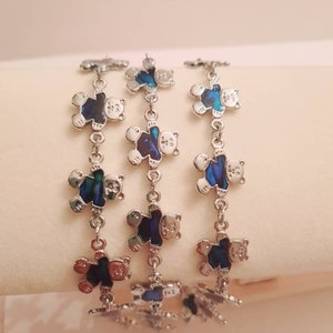 May include: Three silver bracelets with blue and green iridescent bear charms. The bears are facing forward with their arms raised.